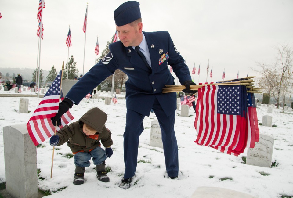 Before-the-Veterans-Day-ceremony-at-Fort-George-Wright-Cemetery-in-Spokane-Wash.-Master-Sergeant-Jason-Young-from-Fairchild-Air-Force-Base-with-his-son-Cooper-place-American-flags-next-to-gravestones-of-US-military-veterans-o-960x649